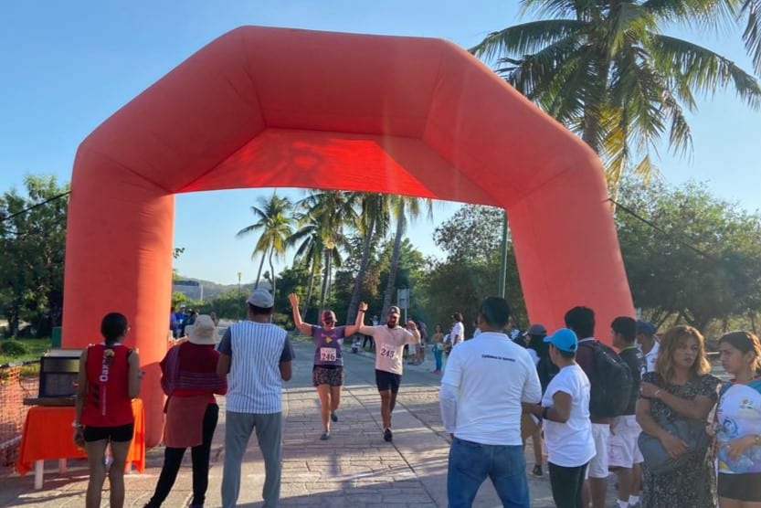 Shev crossing the finish line under an orange inflatable ending a 5k race in Huatulco