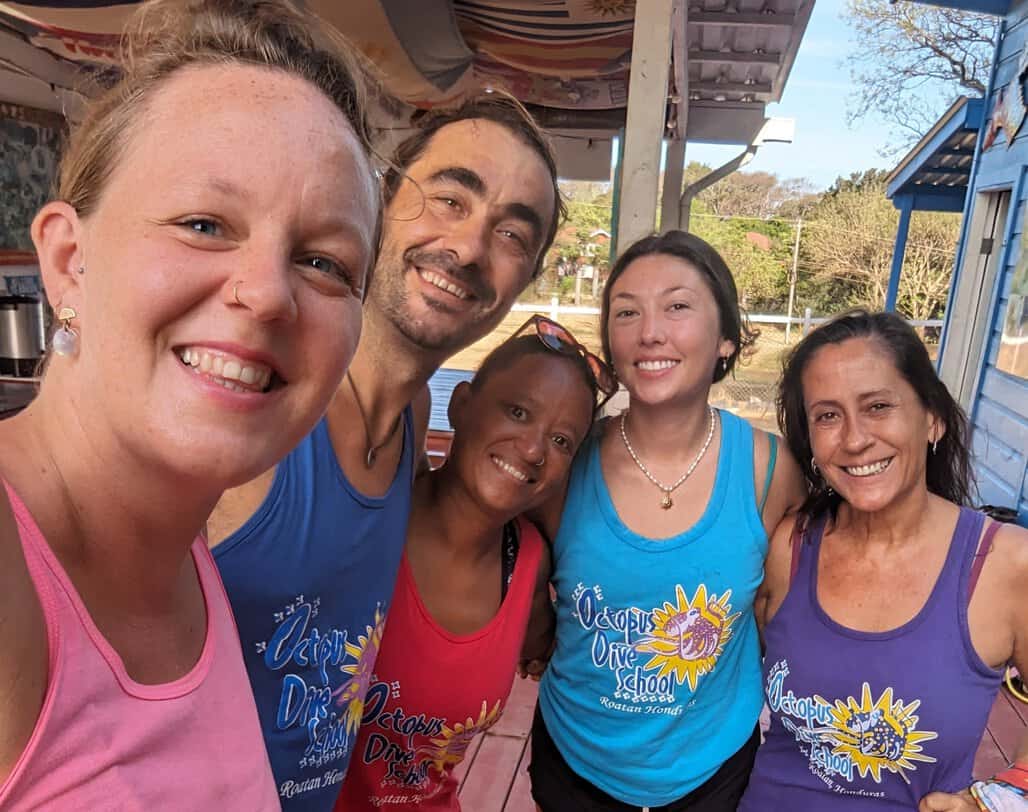 5 smiling dive masters and instructors from Octopus dive school in Roatan wear matching colourful tshirts from one of Roatan's best dive shops