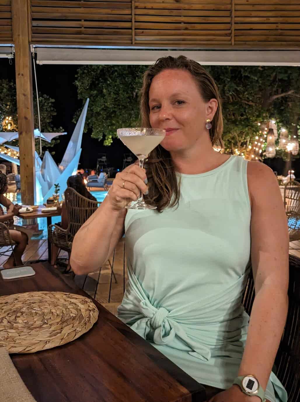 Shev, with her hair down and sporting a light green dress, enjoys a specialty cocktail at Ibagari on their patio