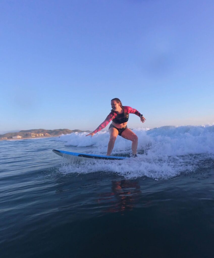 shev surfs a small wave in cerritos, baja during golden hour. The sky is a brilliant blue behind her