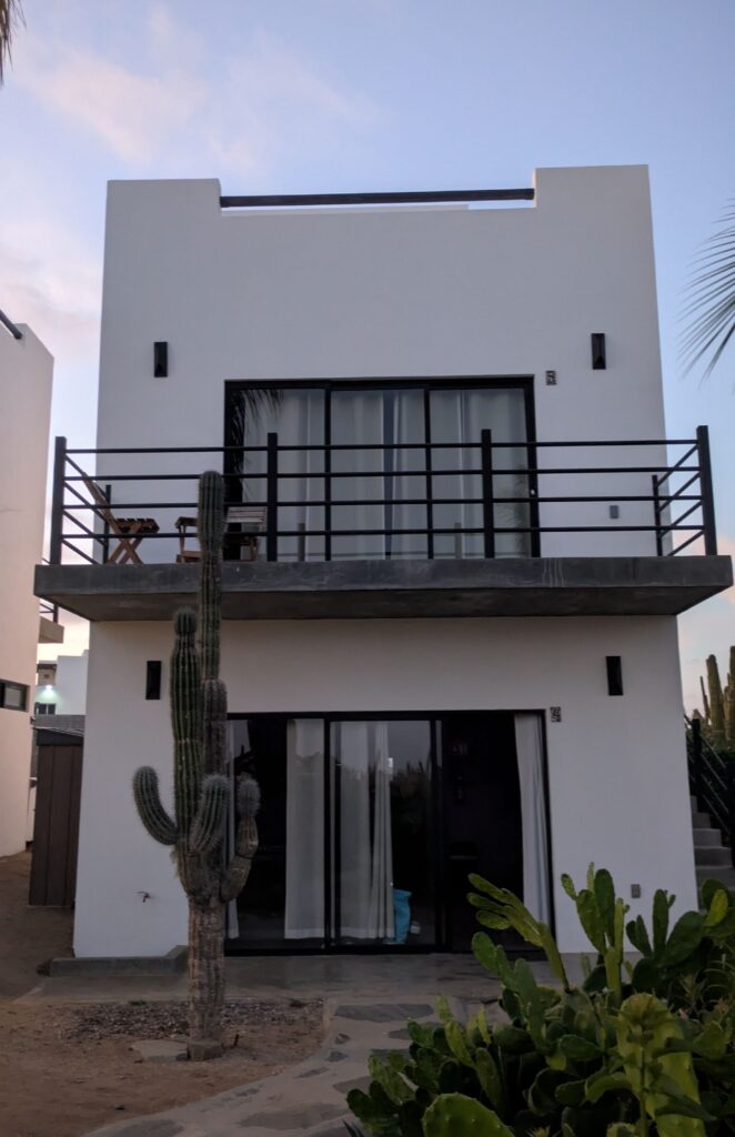 a white, two story building occupies the frame. There is a visible rooftop patio, and balcony on the second floor